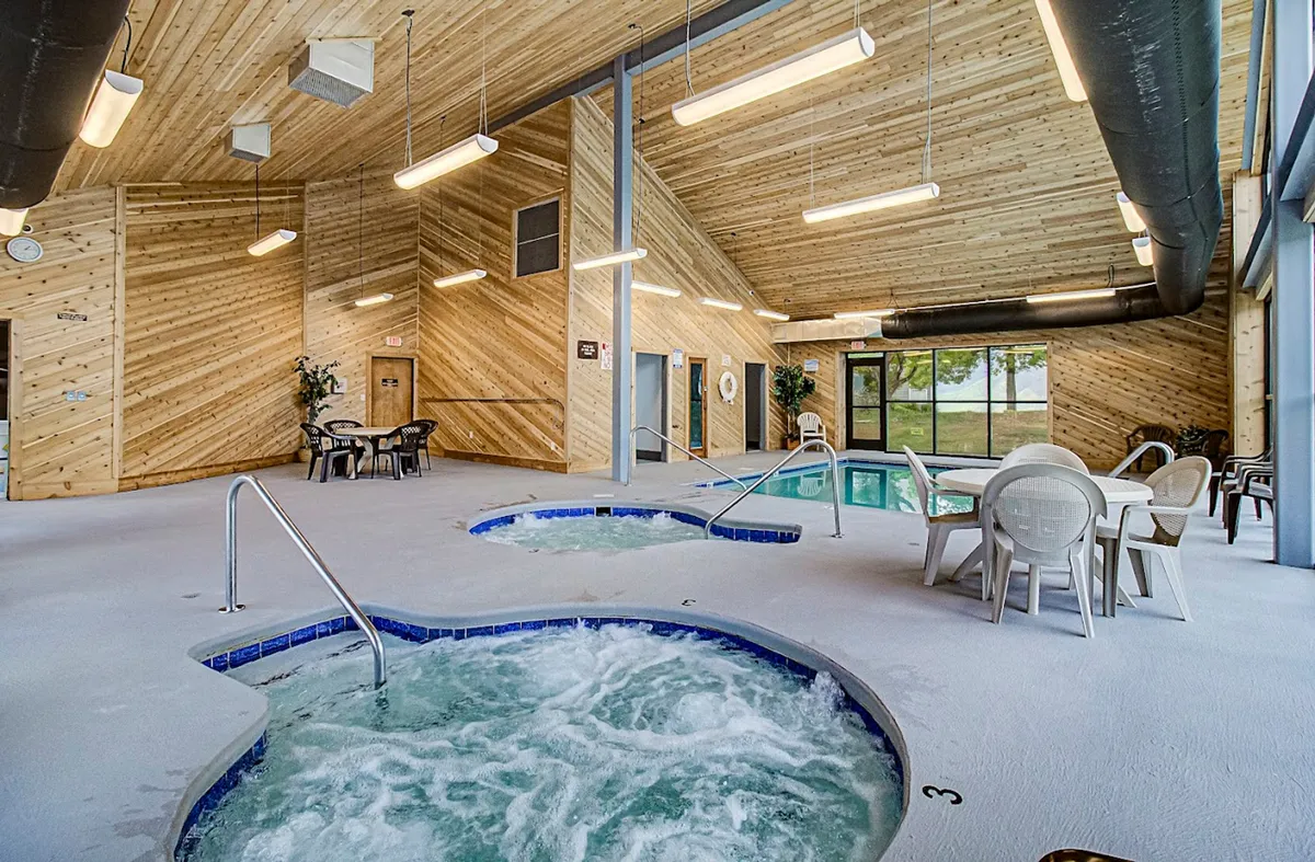 A spacious indoor area featuring hot tubs, a swimming pool, wooden ceiling, and seating for groups. The setting is calm and rejuvenating, ideal for soaking after a swim or socializing with loved ones in a spa-like ambiance.