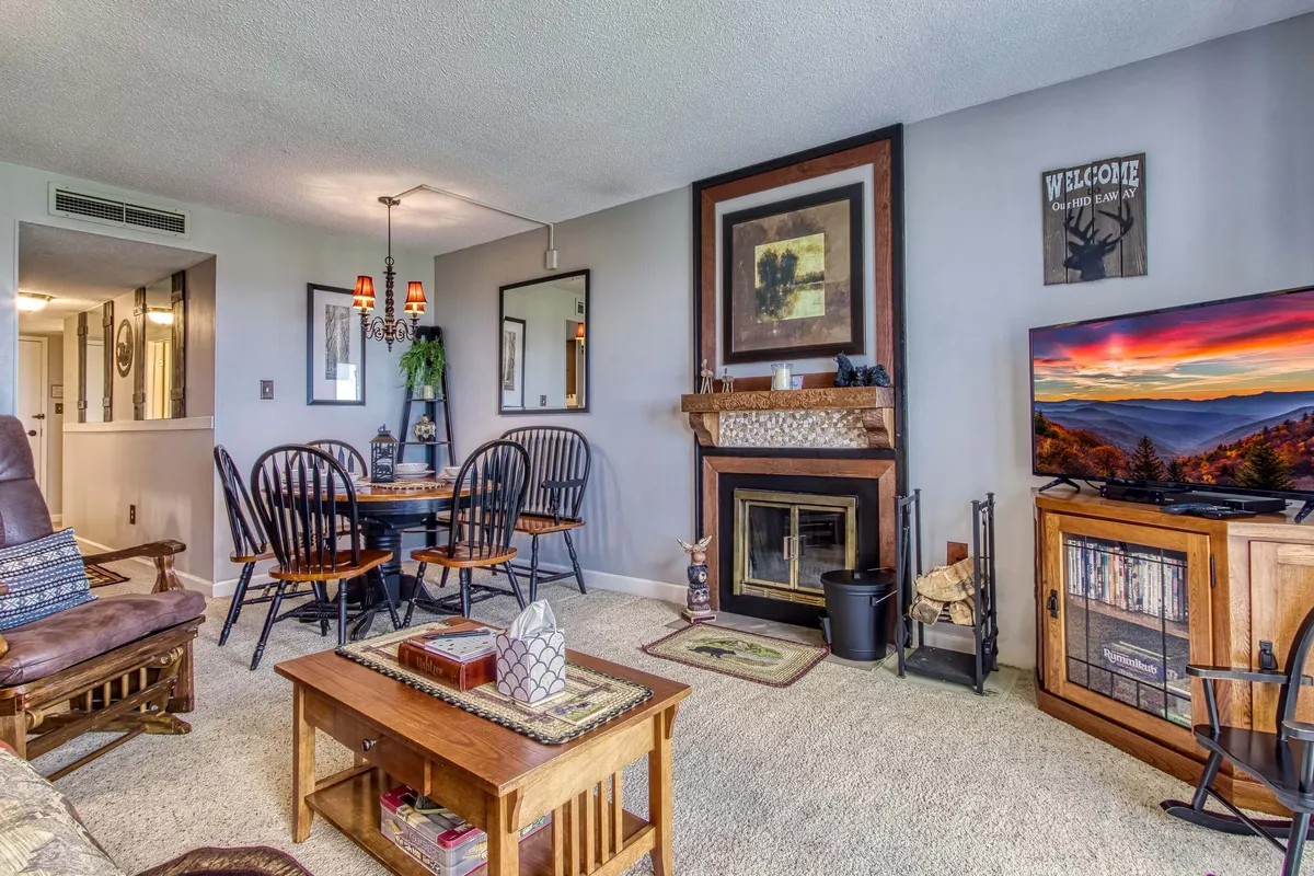 A warm, inviting open-plan living area featuring a cozy fireplace, a large TV for movie nights, a dining table perfect for family gatherings, and tasteful decorative art. Plush seating offers a comfortable spot to unwind, while the space exudes a sense of togetherness ideal for both relaxation and entertaining.