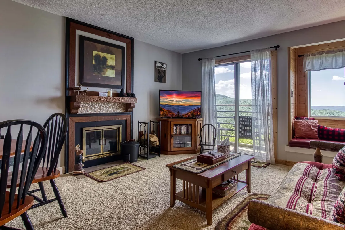 A comfortable living room with a plush seating area facing a fireplace and television, accented by a large window that frames stunning mountain views. The decor is modern yet homey, and the layout invites both relaxation and socializing. Soft lighting enhances the tranquil, welcoming vibe.