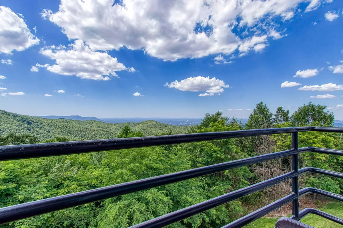 A balcony with a railing framing a stunning mountain range in the background, surrounded by lush greenery. The setting is peaceful, ideal for outdoor dining with breathtaking views.